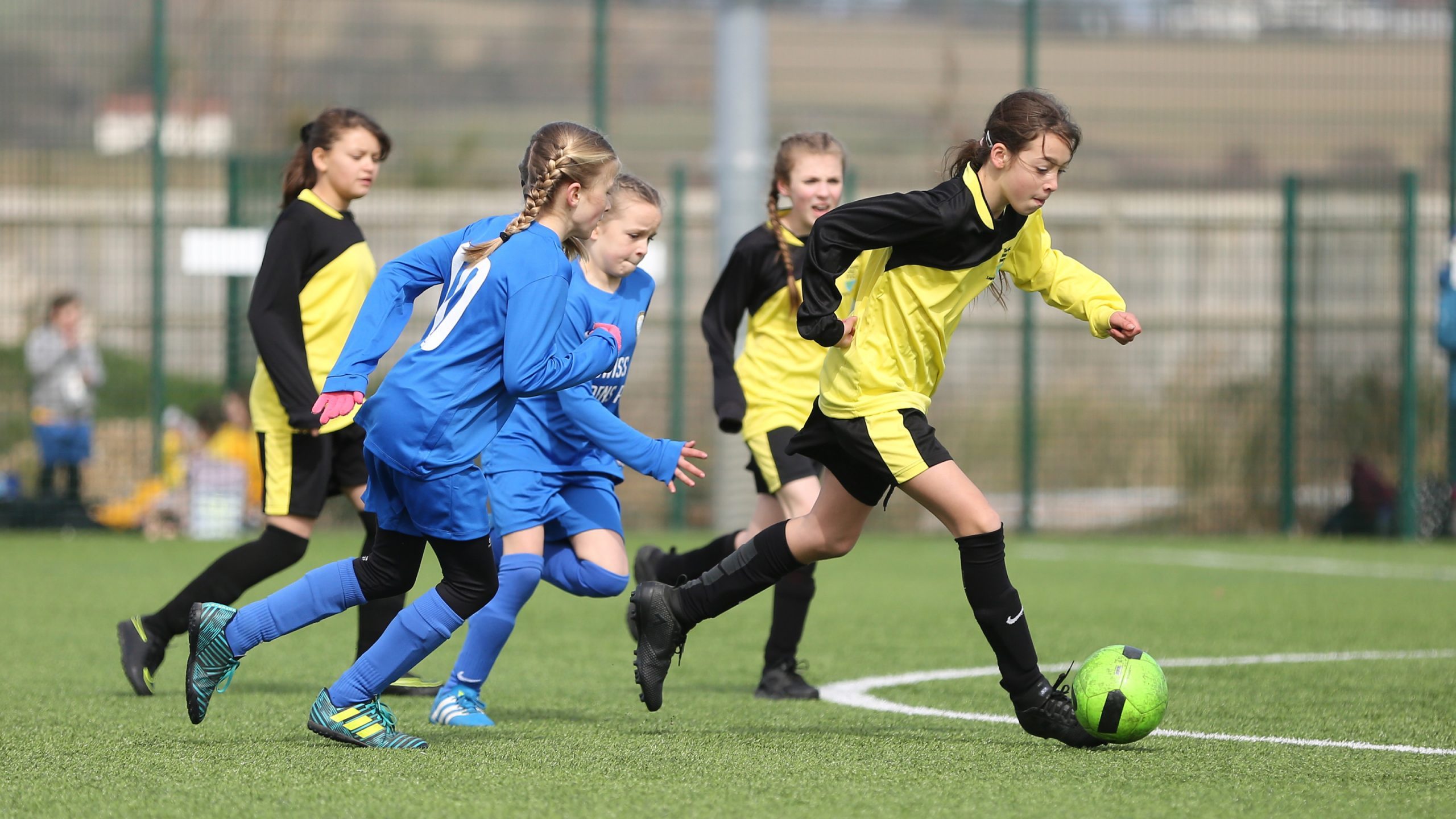 girls playing football in blue and dark and yellow kits